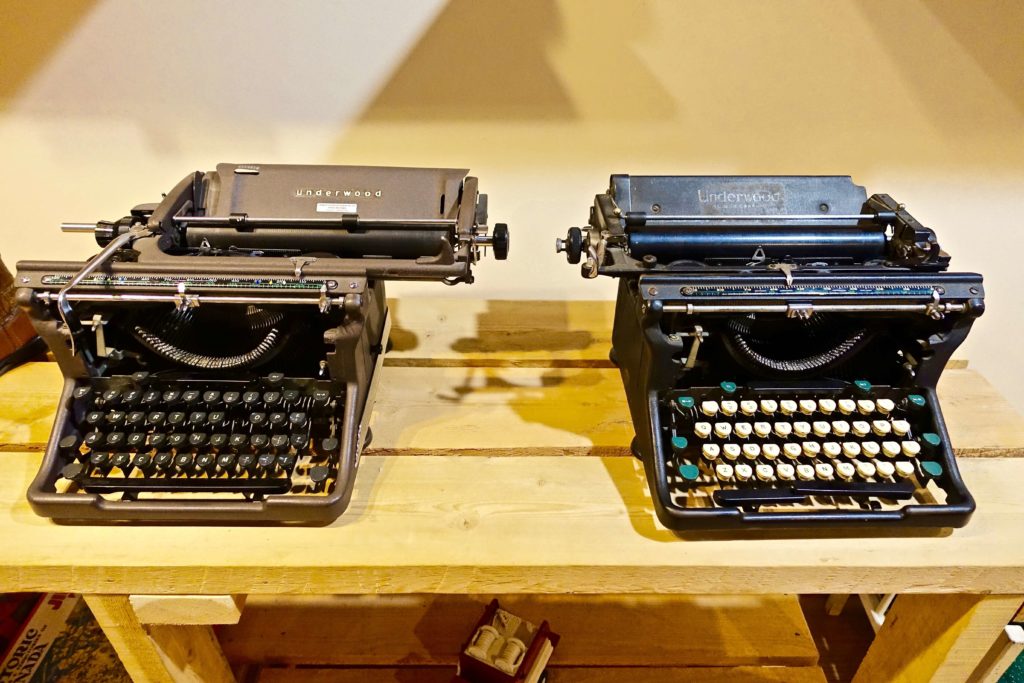 Two old time typewriters on a shelf.